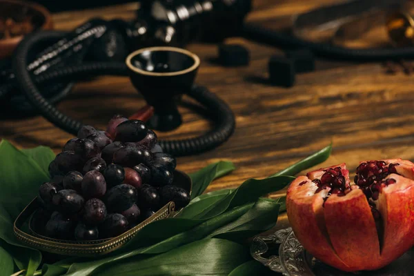 Garnet, grapes, green leaves and hookah on wooden surface — Stock Photo