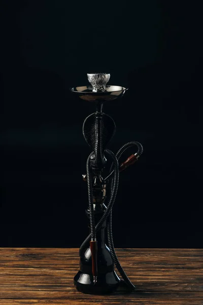 Black hookah stem and hose on wooden surface on black — Stock Photo