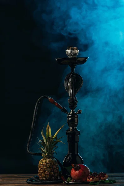 Hookah with exotic fruits on wooden surface in blue smoke — Stock Photo