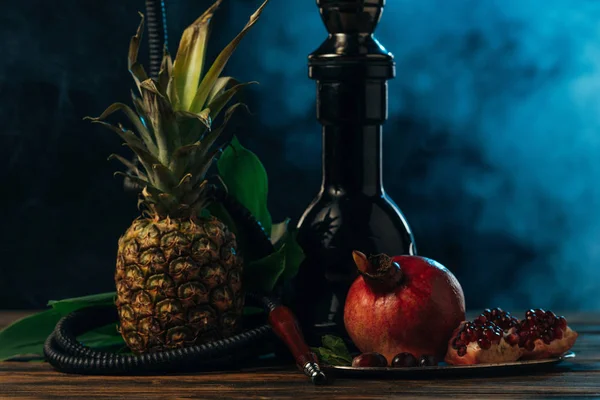 Hookah with exotic fruits on wooden surface in blue smoke — Stock Photo