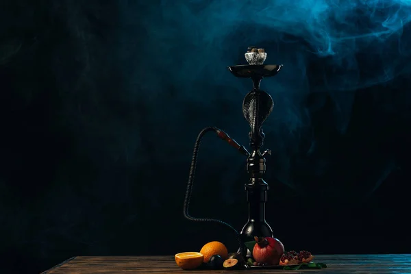 Hookah with exotic fruits on wooden surface in blue smoke — Stock Photo
