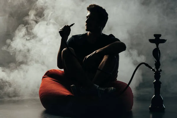 Silhouette de l'homme assis sur une chaise de sac de haricots et fumer narguilé — Photo de stock