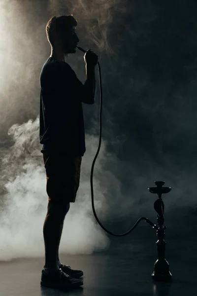 Full length view of silhouette smoking hookah in darkness — Stock Photo