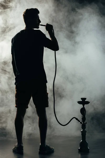 Pleine longueur vue de silhouette fumeur narguilé dans l'obscurité — Photo de stock