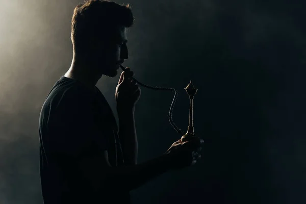 Silhouette eines Mannes, der in der Dunkelheit Wasserpfeife raucht — Stockfoto