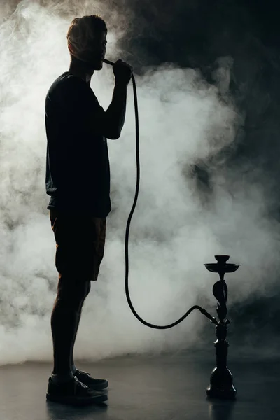 Pleine longueur vue de silhouette fumeur narguilé dans l'obscurité — Photo de stock