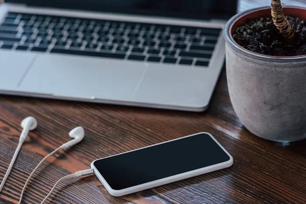 Smartphone com tela em branco, fones de ouvido e laptop na mesa de madeira — Fotografia de Stock