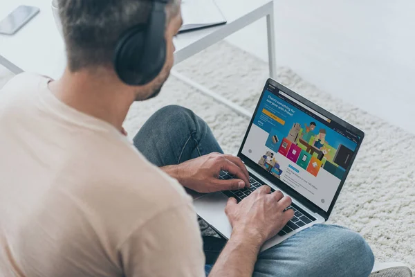 Kyiv, ukraine - 5. Mai 2019: Mann mit Kopfhörer sitzt auf dem Boden und benutzt Laptop mit Amazon-App auf dem Bildschirm. — Stockfoto
