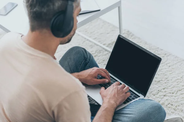 Hombre adulto en auriculares sentados en el suelo y el uso de ordenador portátil con pantalla en blanco - foto de stock