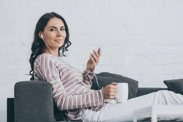 Fröhliche Frau, die in die Kamera schaut, während sie Musik im Kopfhörer hört und in die Kamera schaut — Stockfoto