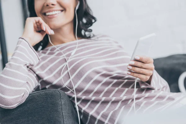 Teilbild einer lächelnden Frau, die ihr Smartphone in der Hand hält, während sie Musik im Kopfhörer hört — Stockfoto