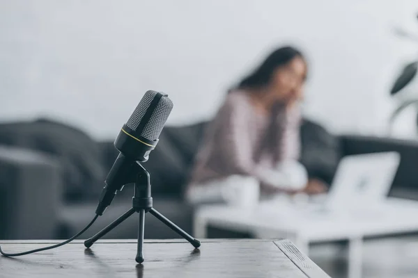 Foyer sélectif du microphone sur la table en bois et la femme assise au bureau près de l'ordinateur portable — Photo de stock