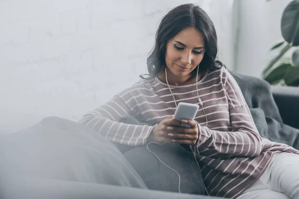 Selective focus of young woman listening music in earphones while using smartphone — Stock Photo