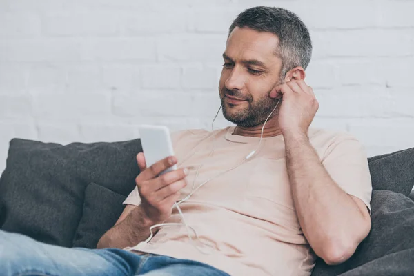 Homem sorrindo usando smartphone enquanto ouve música em fones de ouvido — Fotografia de Stock