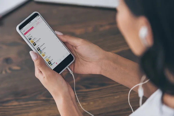 KYIV, UCRANIA - 5 de mayo de 2019: Vista parcial de la mujer en auriculares con teléfono inteligente con aplicación de música de manzana en la pantalla . - foto de stock