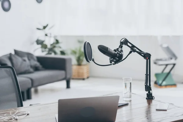 Micropohone, laptop e bicchiere d'acqua su tavolo in legno in studio radio — Foto stock