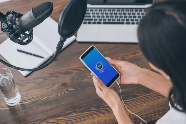 KYIV, UKRAINE - MAY 5, 2019: Cropped view o woman holding smartphone with Shazam app on screen near microphone and laptop. — Stock Photo