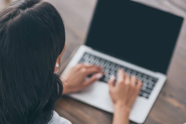 Overhead view of young woman in earphones using laptop while sitting at wooden table — Stock Photo