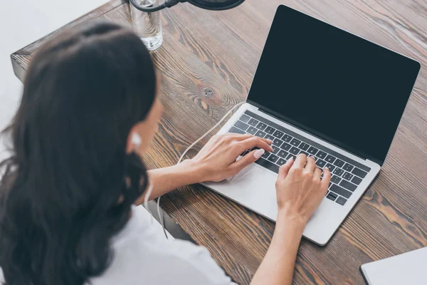 Overhead view of woman in earphones using laptop while sitting at wooden desk — Stock Photo