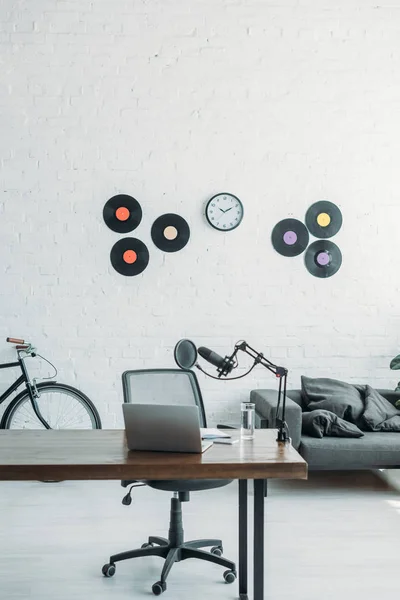 Geräumiges Sendestudio mit Mikrofon und Laptop auf Holztisch, Bürostuhl, Schallplatten und Uhr an weißer Wand — Stockfoto