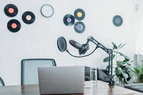 Микрофон, ноутбук и стакан воды на деревянном столе в студии вещания — стоковое фото
