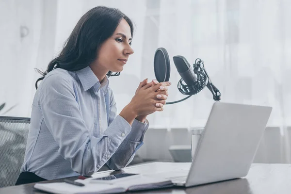 Jolie animateur de radio assis sur le lieu de travail près du microphone et ordinateur portable dans le studio de radiodiffusion — Stock Photo