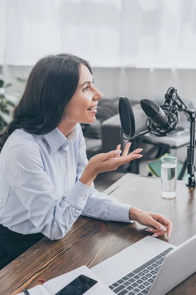 Ospite radio sorridente parlando in microfono mentre seduto alla scrivania vicino al computer portatile in studio di trasmissione — Foto stock