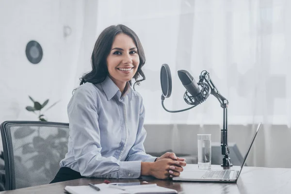 Fröhlicher Radiomoderator lächelt in die Kamera, während er am Arbeitsplatz neben dem Mikrofon sitzt — Stockfoto