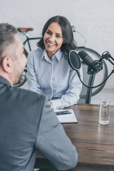 Selective focus of smiling radio host interviewing businessman in broadcasting studio — Stock Photo