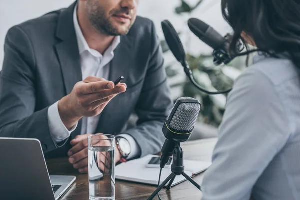 Cropped view of radio host gesturing while interviewing businesswoman in broadcasting studio — Stock Photo