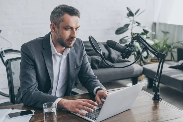 Schöner Radiomoderator mit Laptop am Arbeitsplatz in der Nähe des Mikrofons — Stockfoto