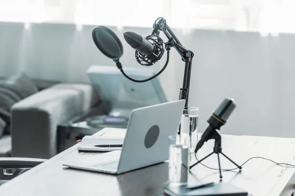 Lugar de trabajo con micrófonos, laptop, portátiles y vasos con agua en estudio de radiodifusión - foto de stock