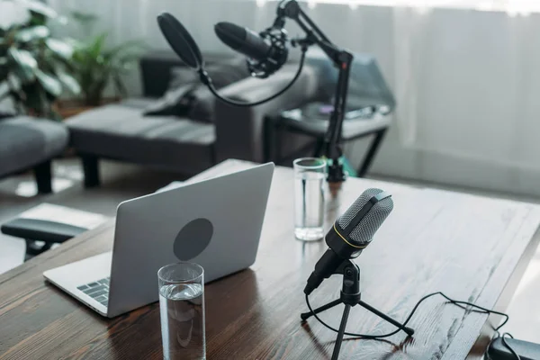 Espaço de trabalho com microfones, laptop e copos de água no estúdio de radiodifusão — Fotografia de Stock