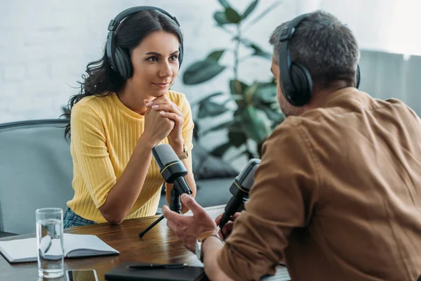Beautiful attentive radio host looking at colleague while sitting at workplace in radio studio — Stock Photo