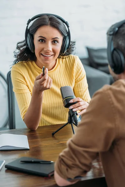 Pretty radio host gesturing and looking at camera while sitting near colleague in broadcasting studio — Stock Photo