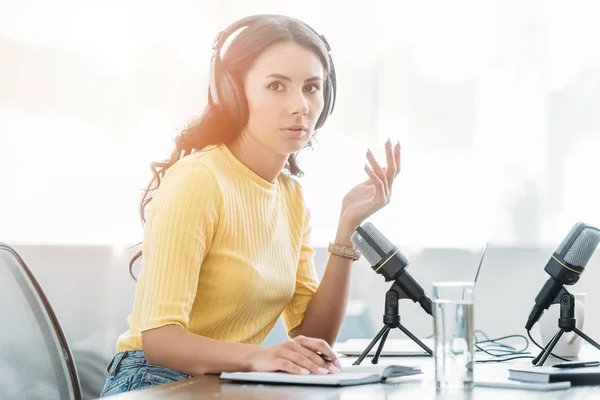 Anfitrião de rádio grave atraente em fones de ouvido gesticulando enquanto olha para a câmera — Fotografia de Stock