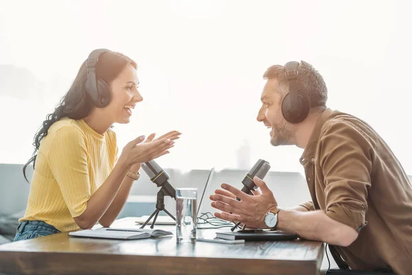 Dos alegres anfitriones de radio hablando y haciendo gestos mientras graba podcast en el estudio - foto de stock