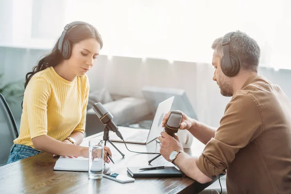 Two serious radio hosts talking while sitting at workplace in radio studio — Stock Photo