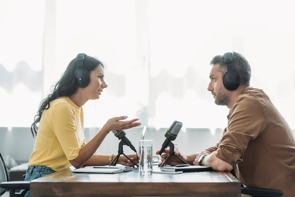 Dos anfitriones de radio serios en auriculares hablando mientras está sentado en el lugar de trabajo en el estudio - foto de stock