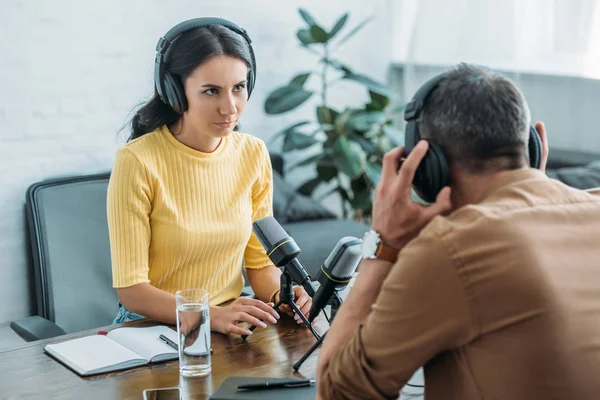 Attractive serious radio host looking at colleague while sitting at workplace in studio — Stock Photo