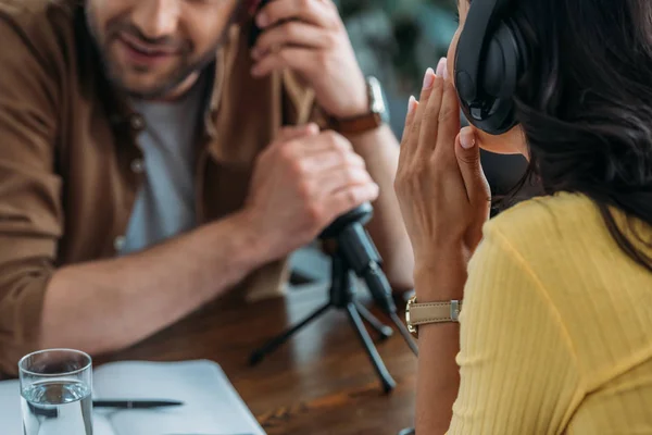 Vista parcial del anfitrión de radio que cubre el micrófono con la mano mientras está sentado cerca de un colega que susurra - foto de stock