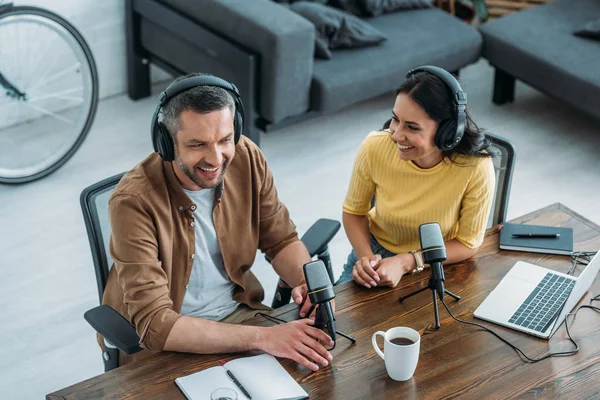 Two cheerful radio hosts talking while sitting at workplace in broadcasting studio — Stock Photo