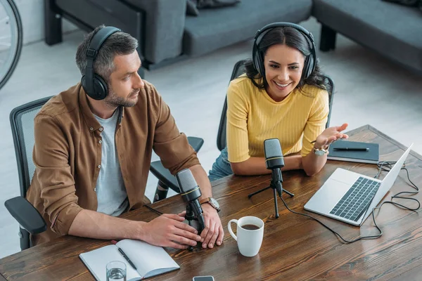 Pretty radio hosts talking in microphone while sitting at workplace near colleague — Stock Photo