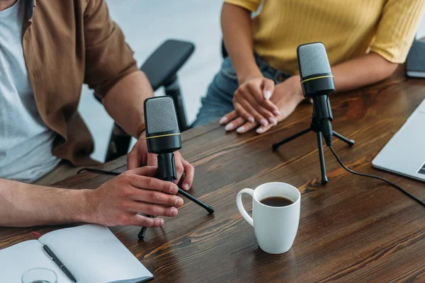Cropped view of two radio hosts sitting at workplace near microphones — Stock Photo