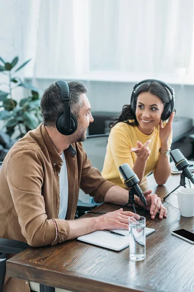 Cheerful radio host pointing with finger while sitting near colleague in broadcasting studio — Stock Photo