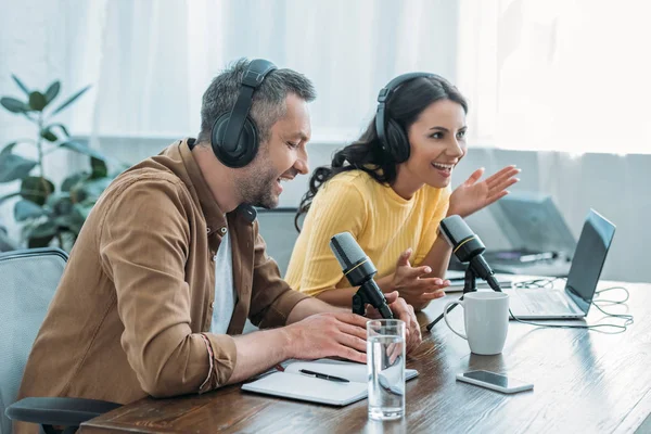 Two cheerful radio hosts in headphones recording podcast in studio — Stock Photo