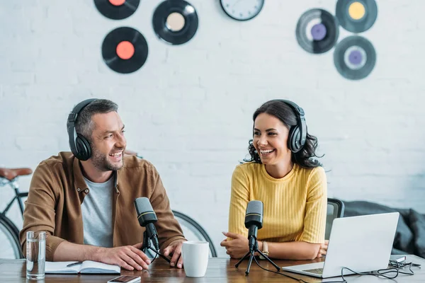 Two cheerful radio hosts sitting near microphones and recording podcast in studio — Stock Photo