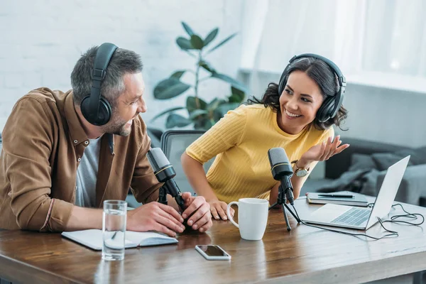 Two radio hosts in headphones laughing while recording podcast in studio together — Stock Photo
