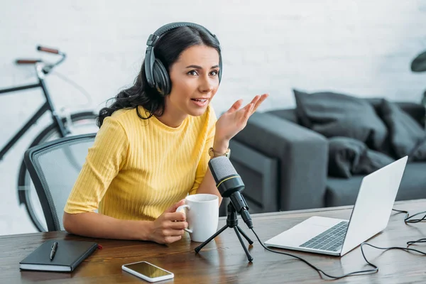 Anfitrião de rádio atraente falando em microfone enquanto segurando xícara de café — Fotografia de Stock