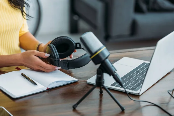 Ausgeschnittene Ansicht des Radiomoderators, der Kopfhörer hält, während er neben dem Mikrofon sitzt — Stockfoto